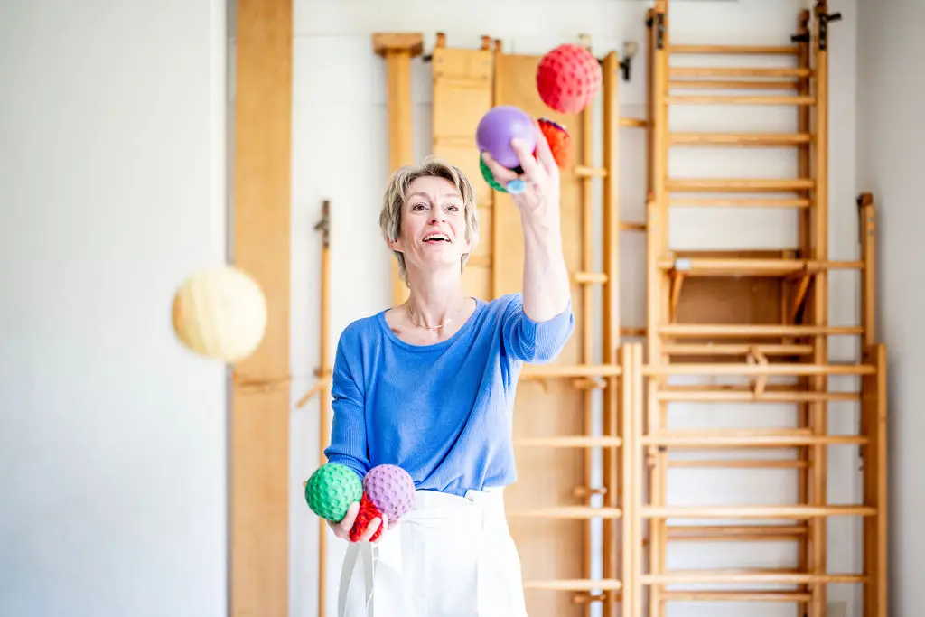 Josanne de Graaf jongleert met gekleurde ballen voor een wandrek in de gymzaal